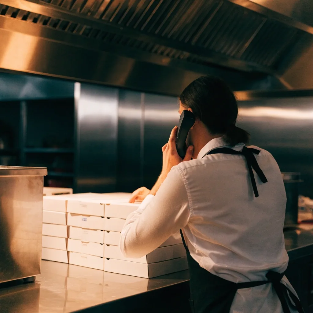 A customer calling the takeaway shop from inside a warm-lit pizza restaurant